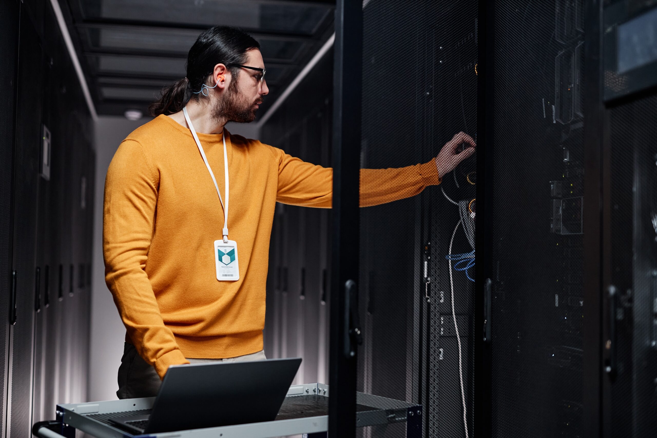 Waist up portrait of bearded network engineer using laptop while working in server room