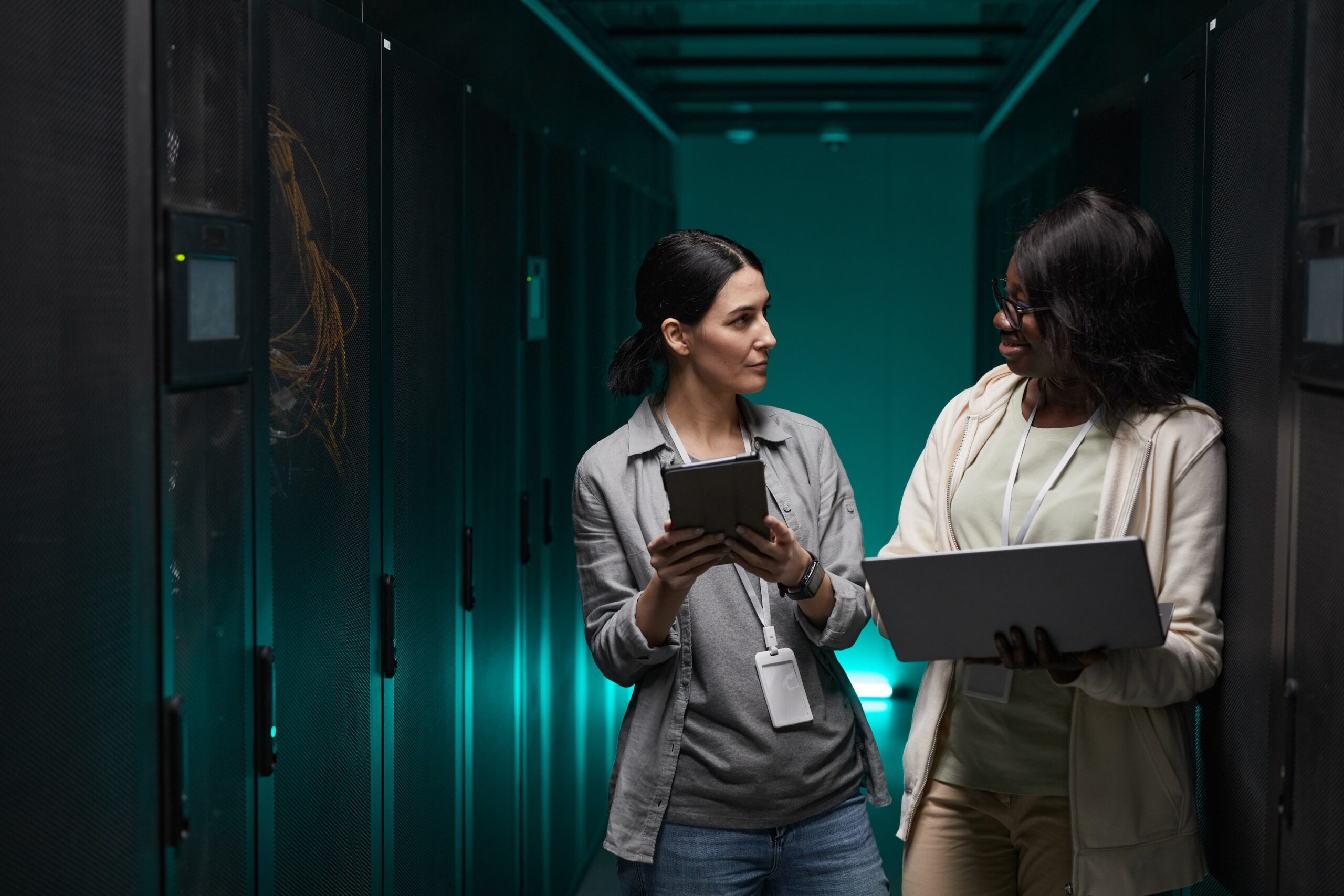 Waist up portrait of two young women using laptop while working with supercomputer in server room, Data backup and recovery concept